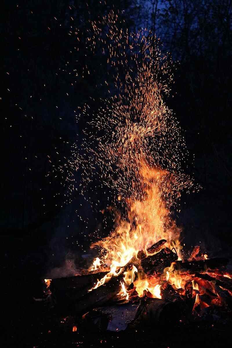 A bonfire with sparks flying into the night sky. - Camping