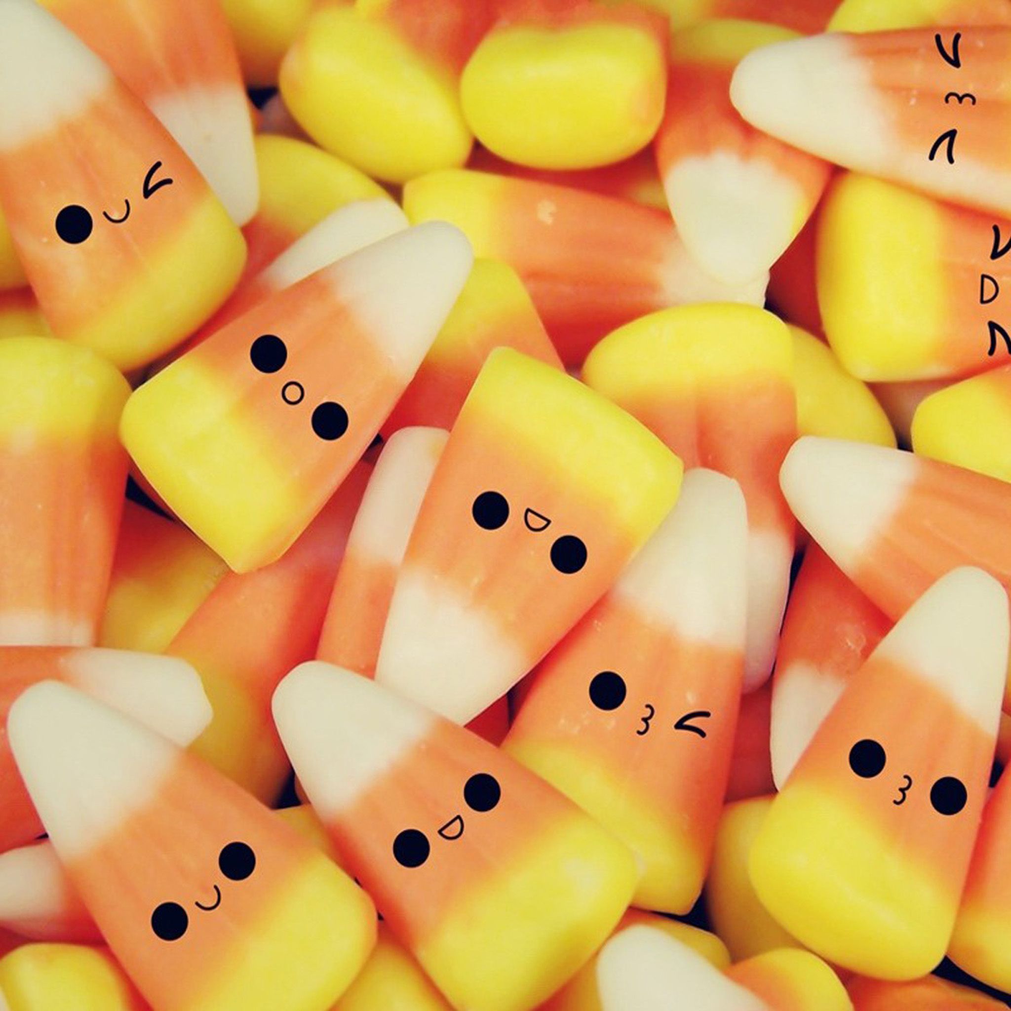 A pile of candy corn with faces drawn on them. - Candy