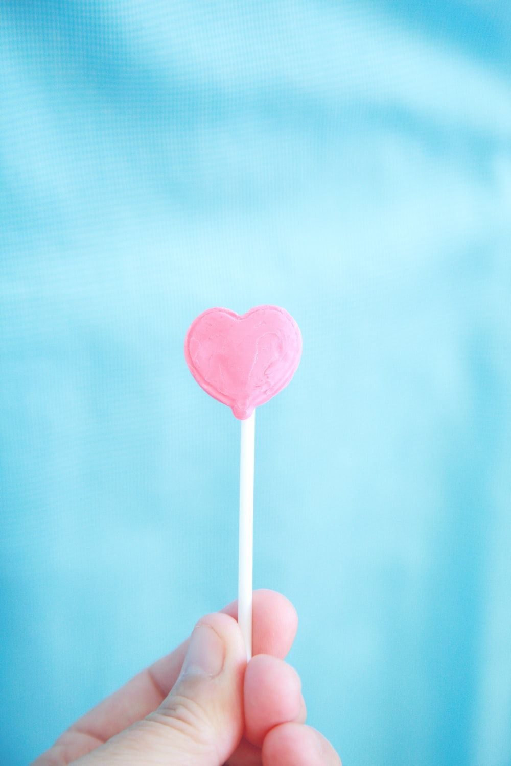 A person holding a pink heart shaped lollipop - Candy