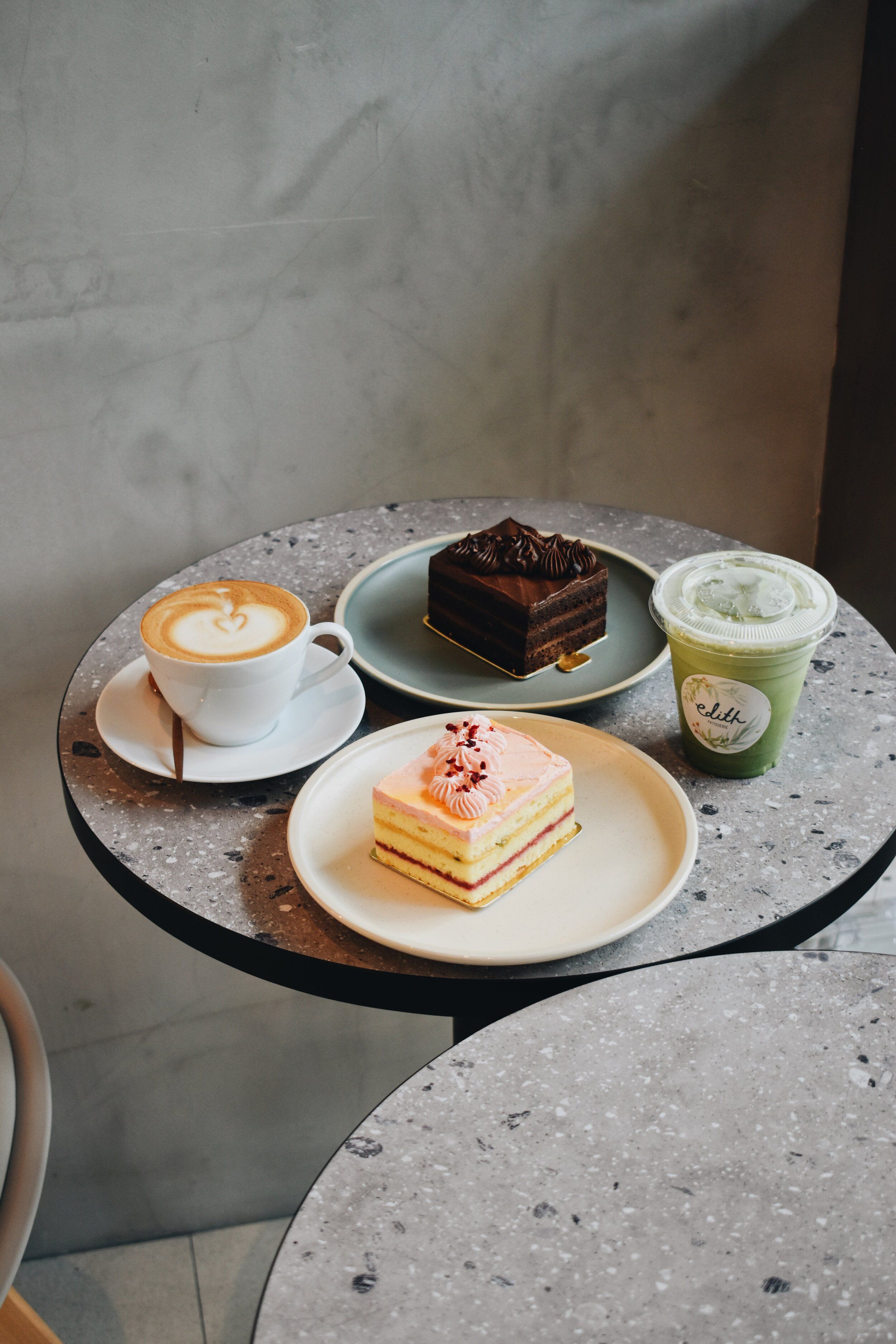 A table with a plate of cake, a cup of coffee, and a cup of green tea. - Bakery