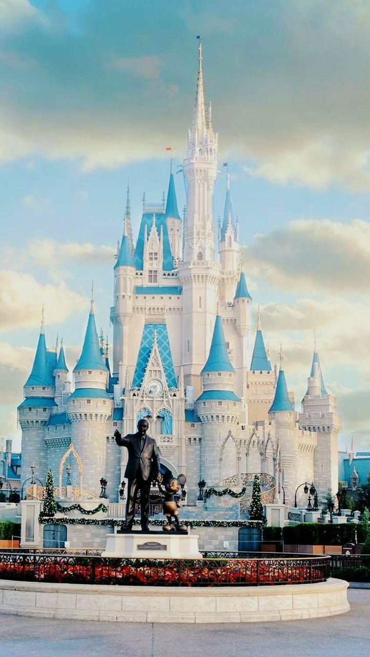 A statue of Walt Disney and Mickey Mouse in front of the iconic Disney castle. - Castle