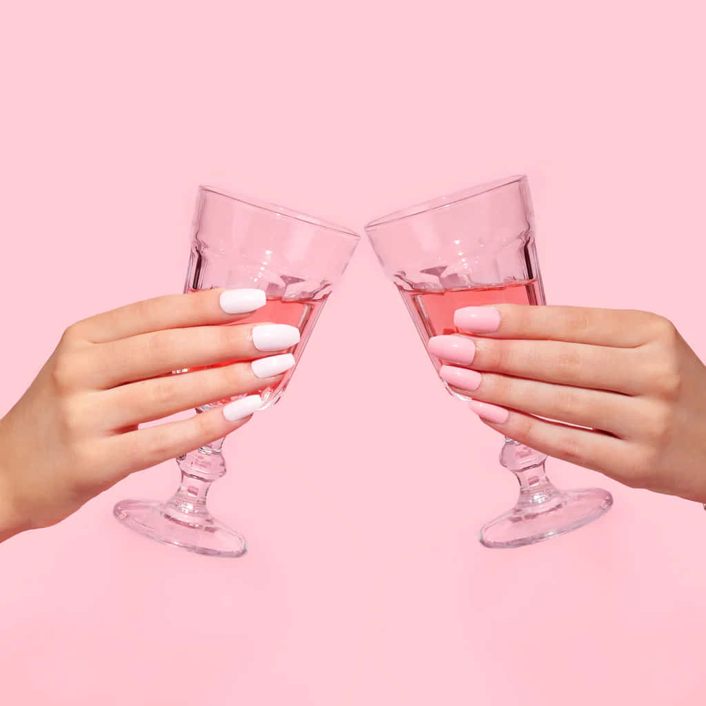 Two hands holding wine glasses with pink wine on a pink background - Champagne