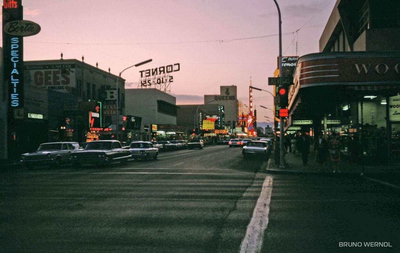 A city street at dusk with cars and neon signs. - Las Vegas