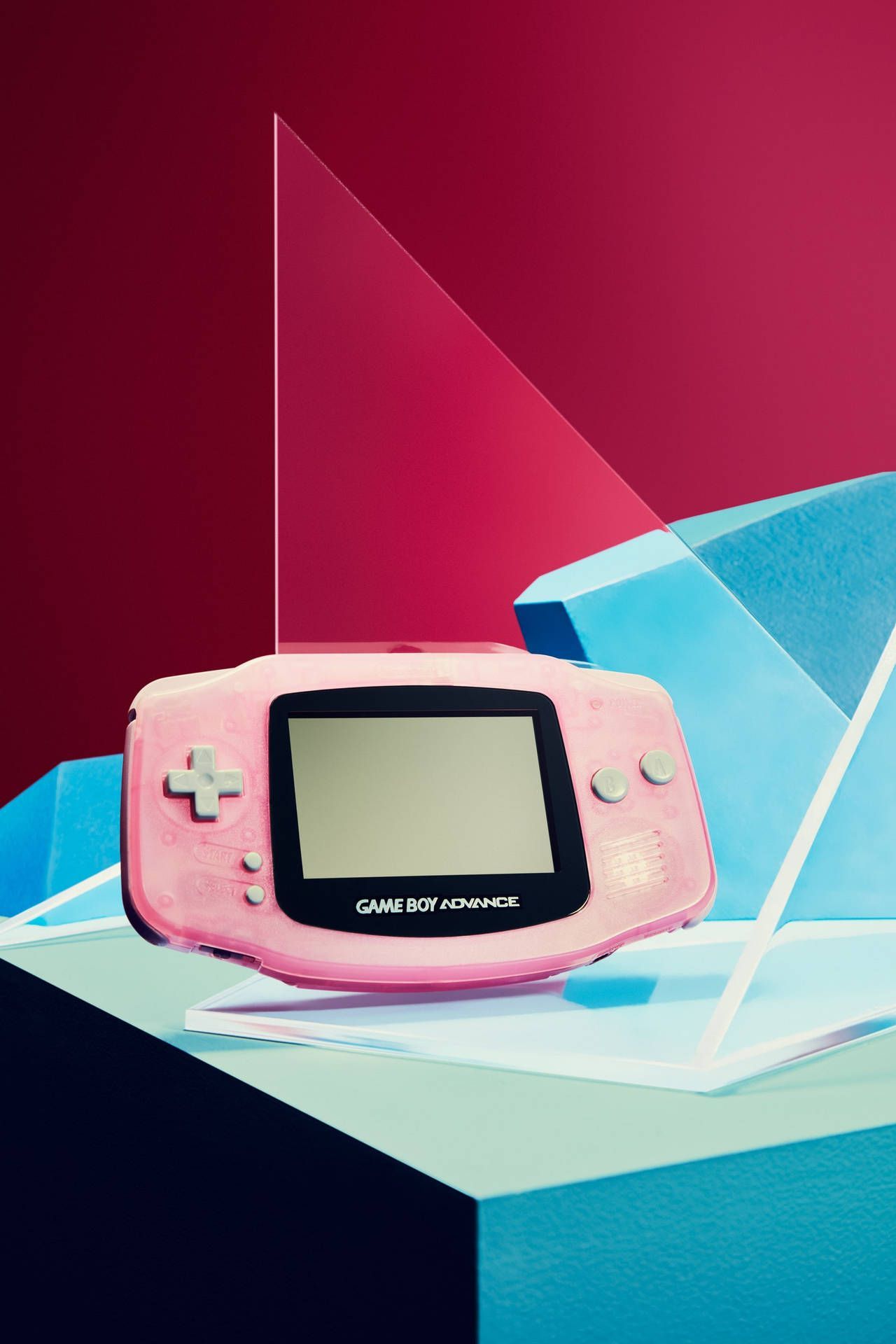 A pink Game Boy Advance sits on a blue and white surface against a red wall. - Game Boy