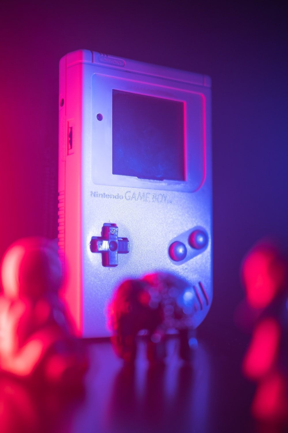 A Gameboy is lit up by red and blue lights. - Game Boy