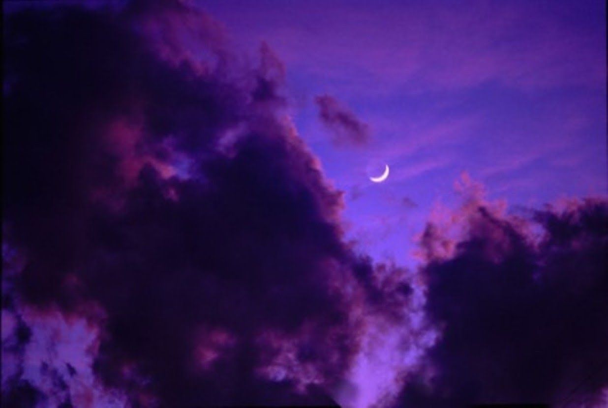 A crescent moon is seen through the clouds in a purple sky. - Computer