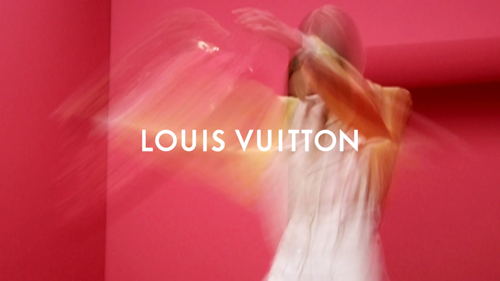 A model is spinning in a white dress in front of a red background. - Louis Vuitton