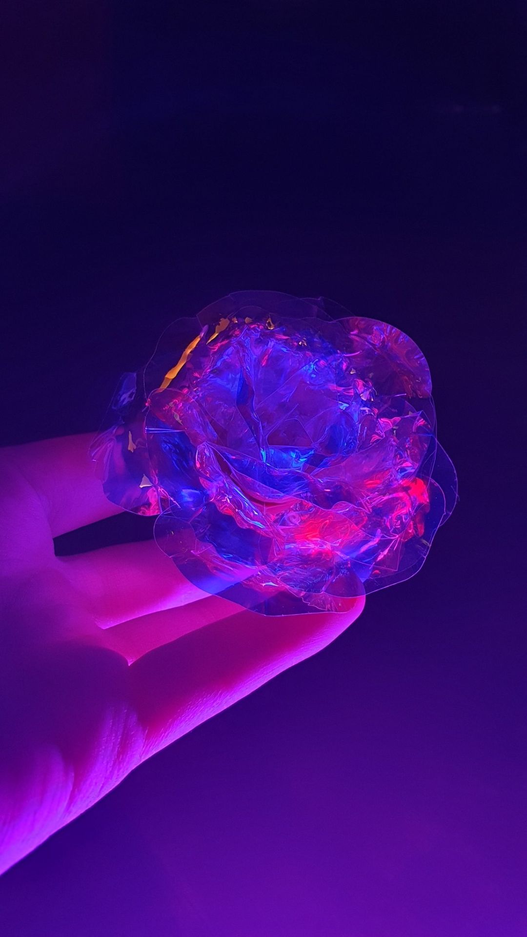 A hand holding a piece of plastic that looks like a flower - Neon purple, dark purple