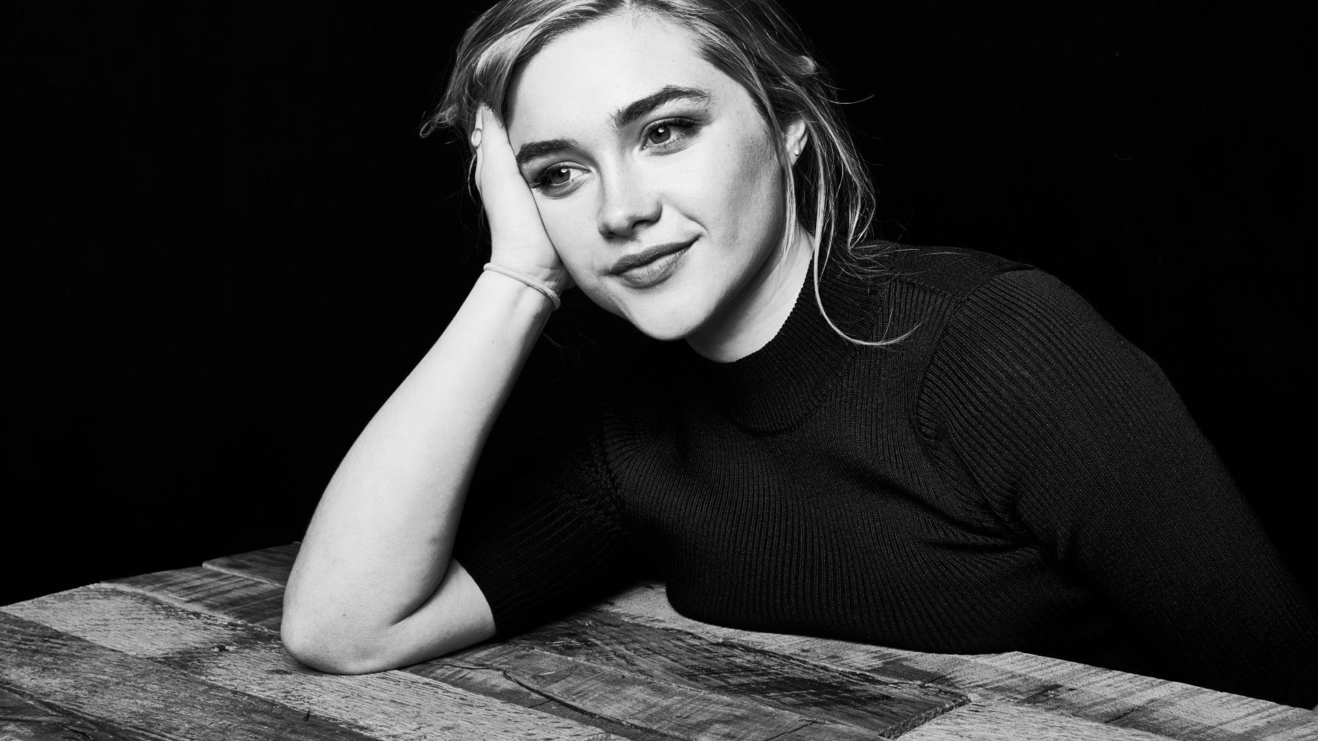 A black and white photo of a woman sitting at a table with her head resting on her hand. - Florence Pugh