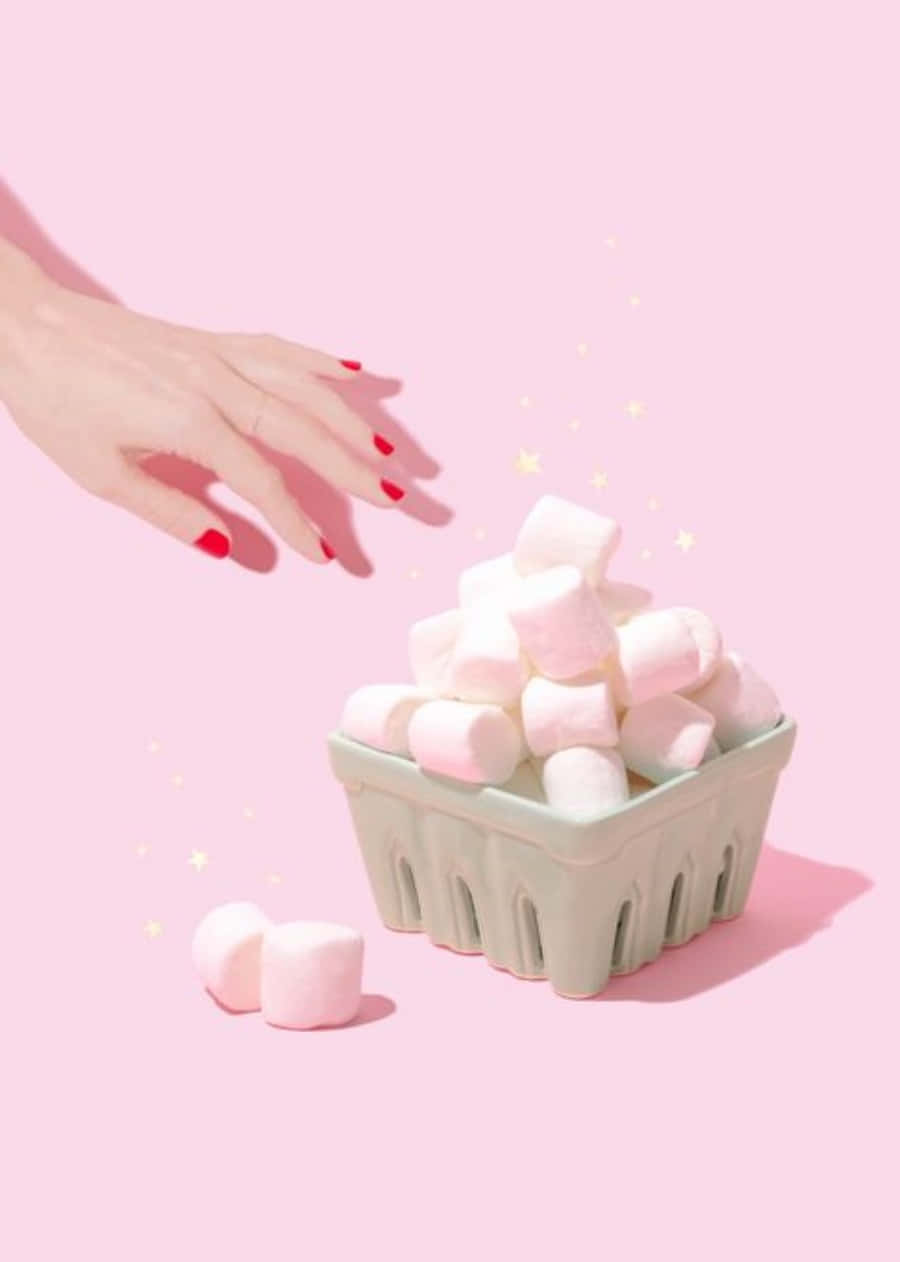 A hand with red nail polish throwing marshmallows into a container. - Marshmallows