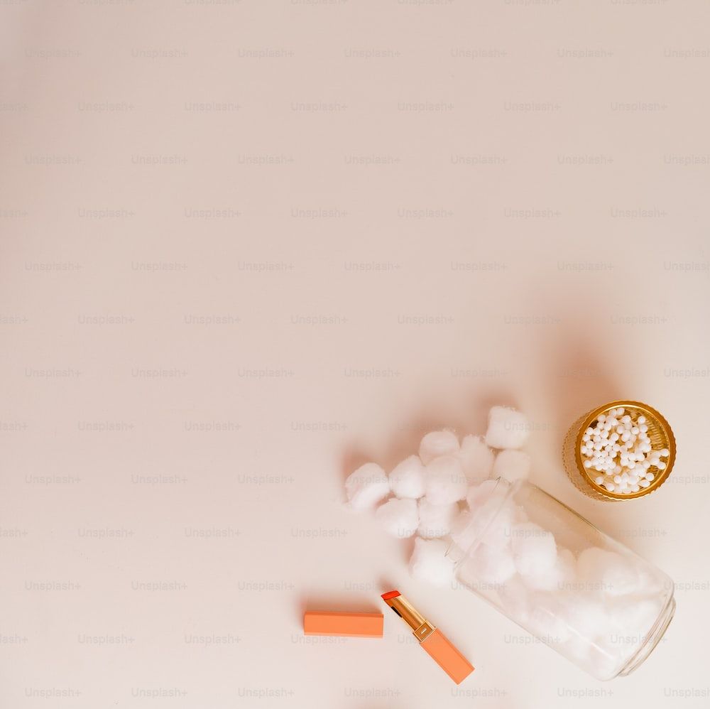 A glass jar of cotton balls and a tube of lipstick on a pink background - Marshmallows