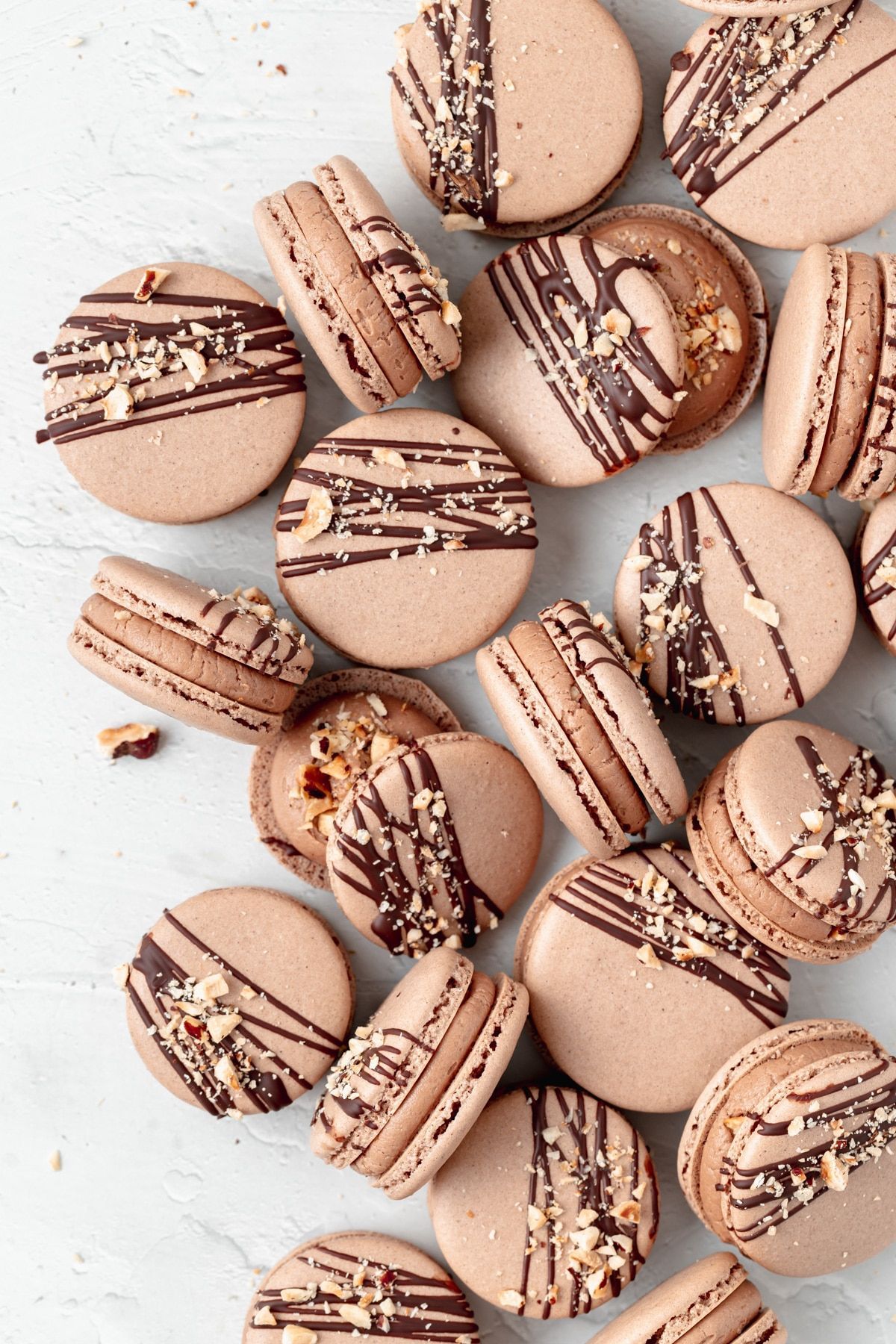 Chocolate macarons with chocolate and caramel drizzle and crushed nuts on a white background - Macarons