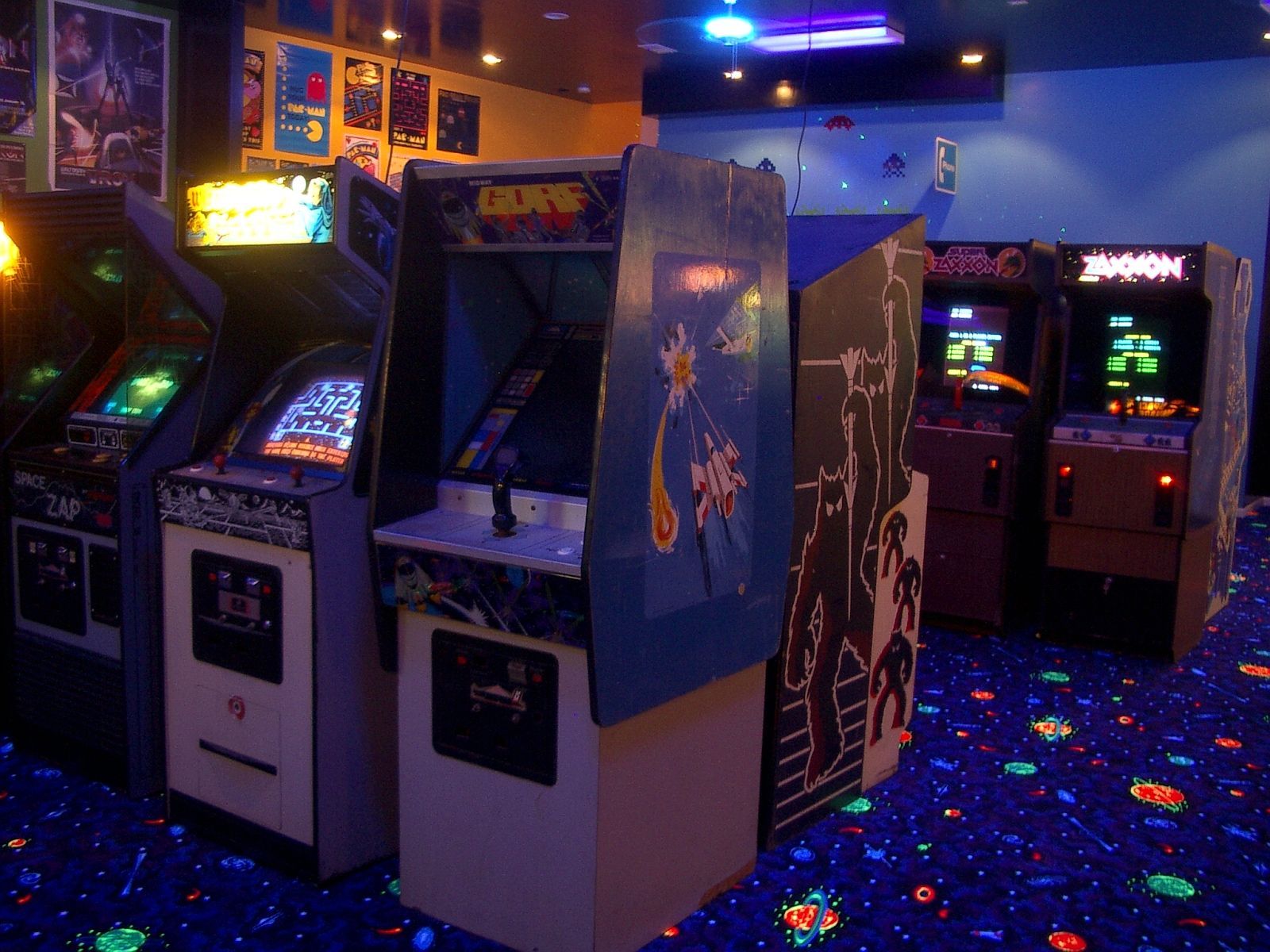 A row of video games are lined up in a dark room. - Arcade