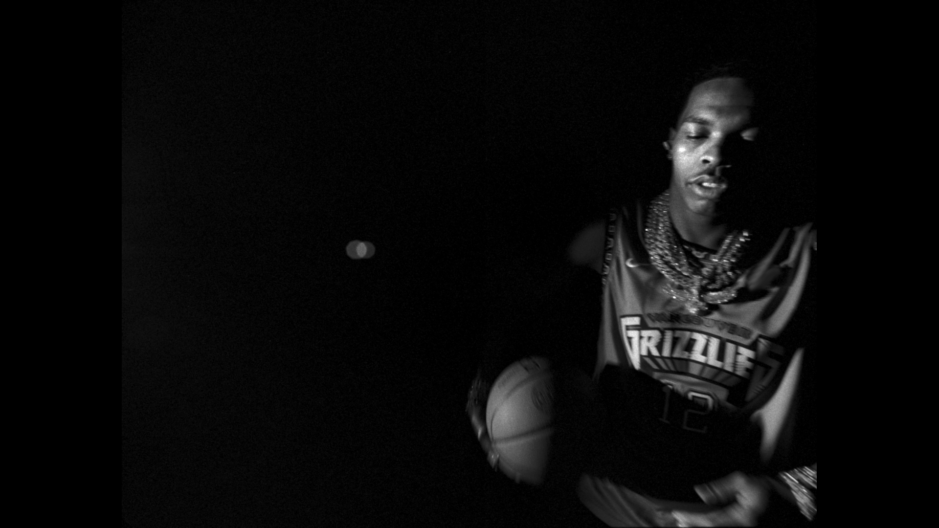 A man in dark clothing holding up his basketball - Ja Morant