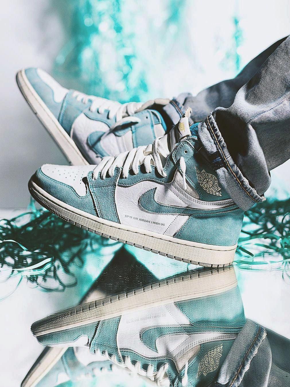 A pair of feet wearing a pair of sneakers with a light blue and white color scheme. - Air Jordan 1