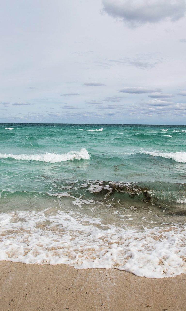 A surfboard sitting on the beach near some waves - Florida, Miami