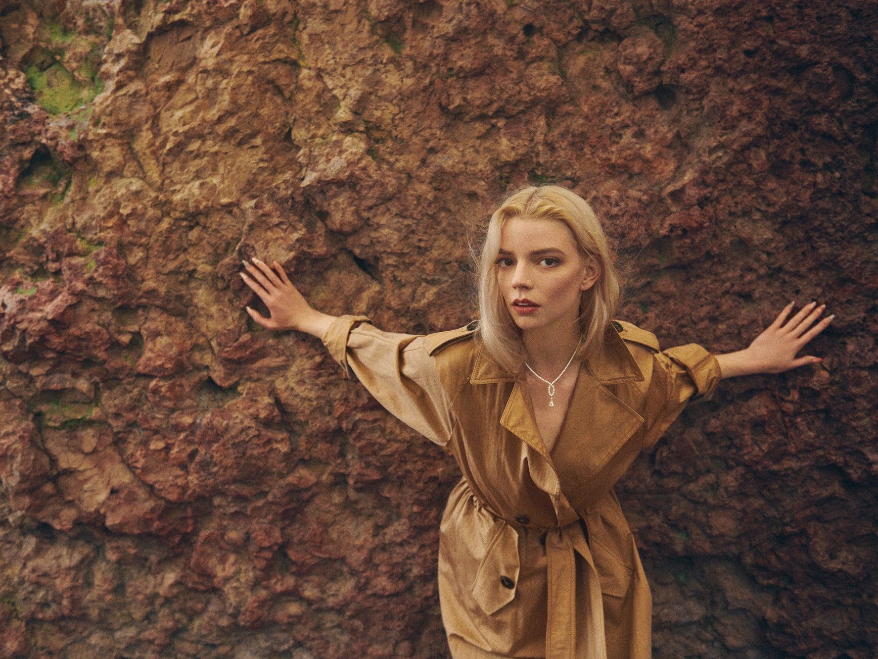 A woman in an overcoat standing against the wall - Anya Taylor-Joy