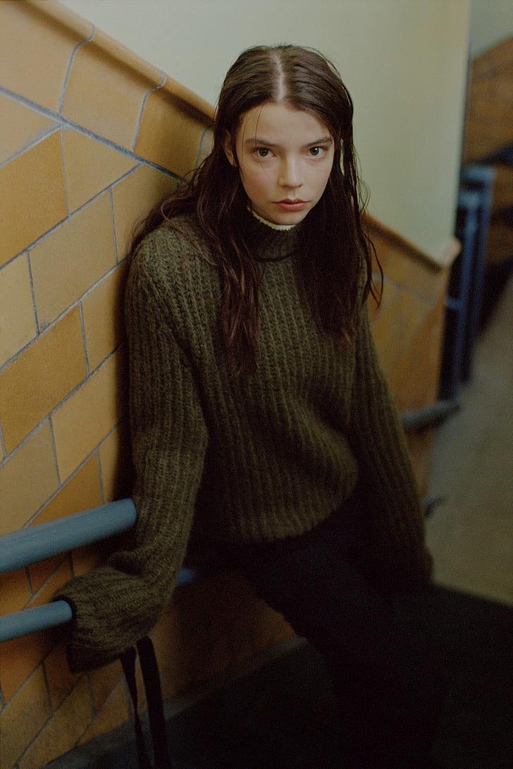 A model with long hair wearing a green turtleneck sweater and black pants. - Anya Taylor-Joy