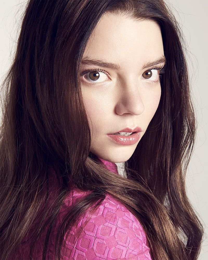 A close up of a woman with long brown hair and a pink top - Anya Taylor-Joy