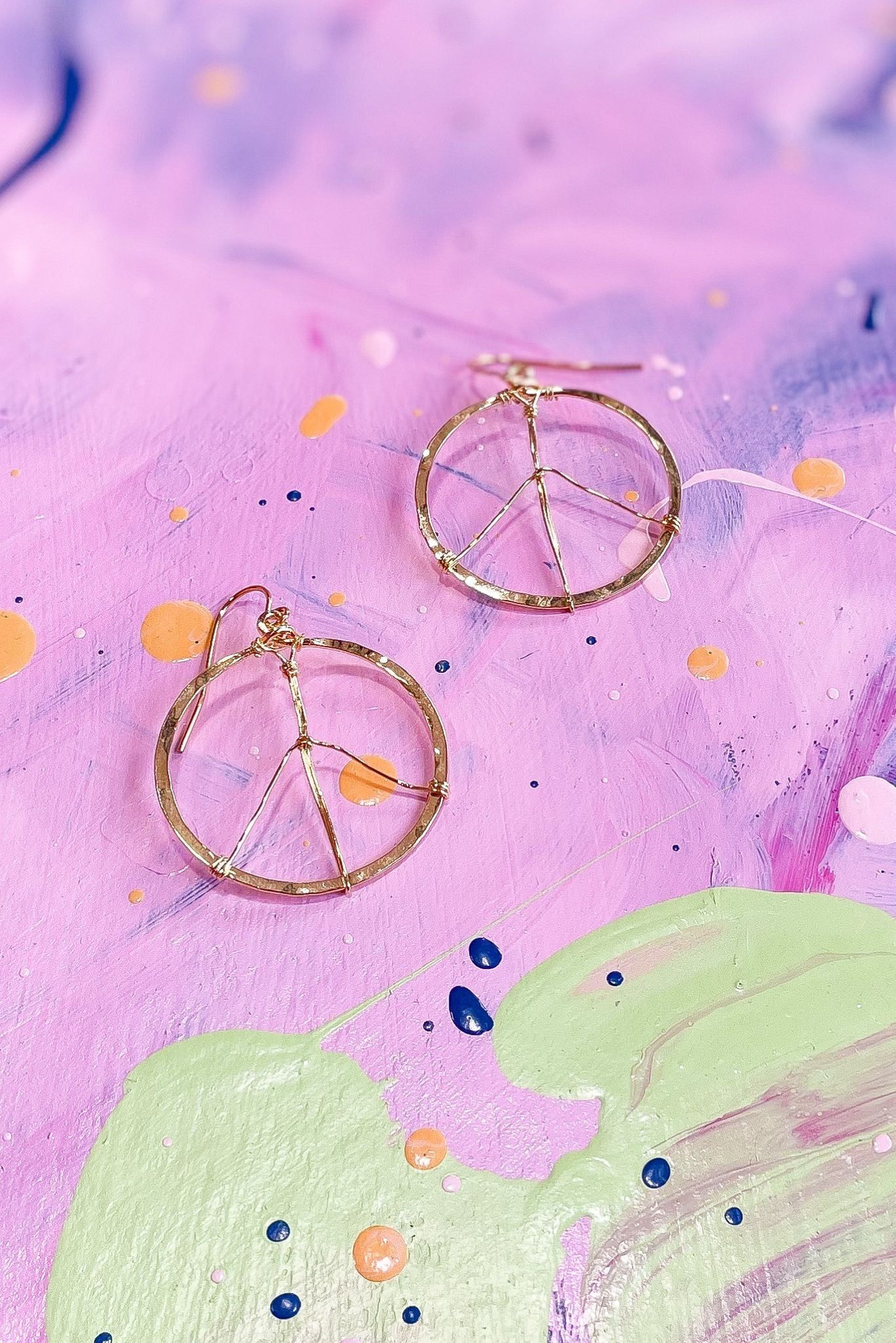A pair of gold peace earrings on top - Peace