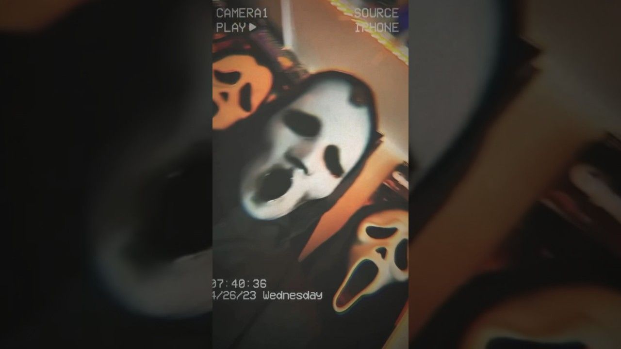 A phone screen displays a picture of a white ghost face mask with orange pumpkin eyes and mouth. - Ghostface