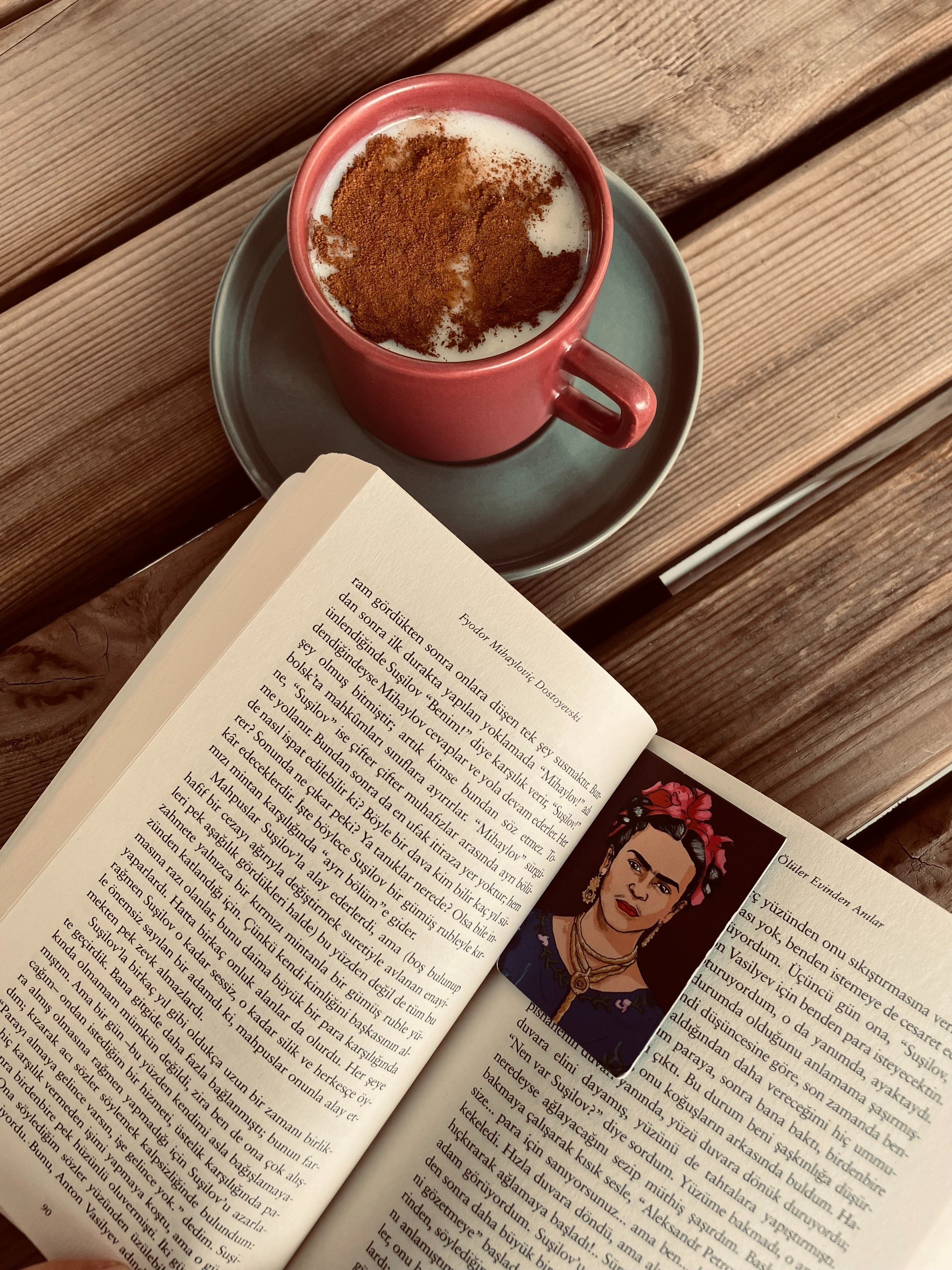 A book open to a page with Frida Kahlo on it, with a cup of coffee on a saucer next to it. - Cozy, Frida Kahlo, books