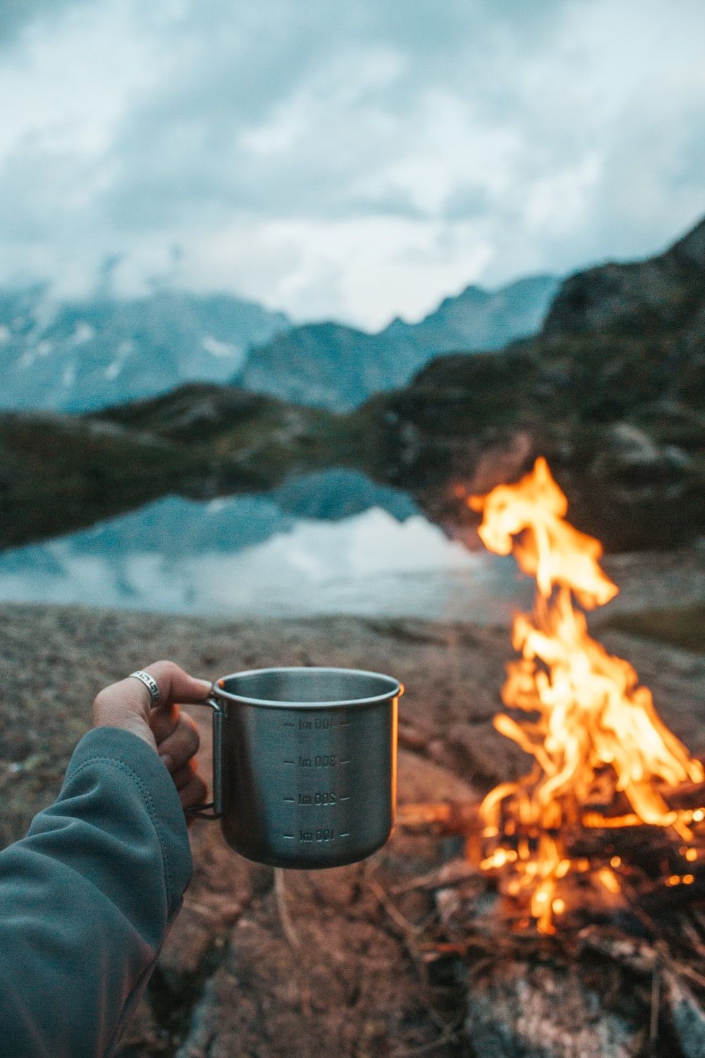 A person holding up an empty cup over the fire - Camping