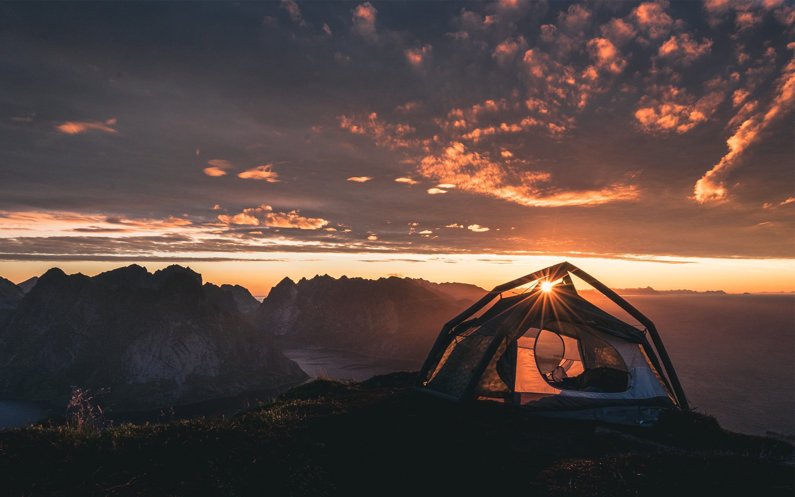 A tent on a mountain top with the sun rising in the background - Camping