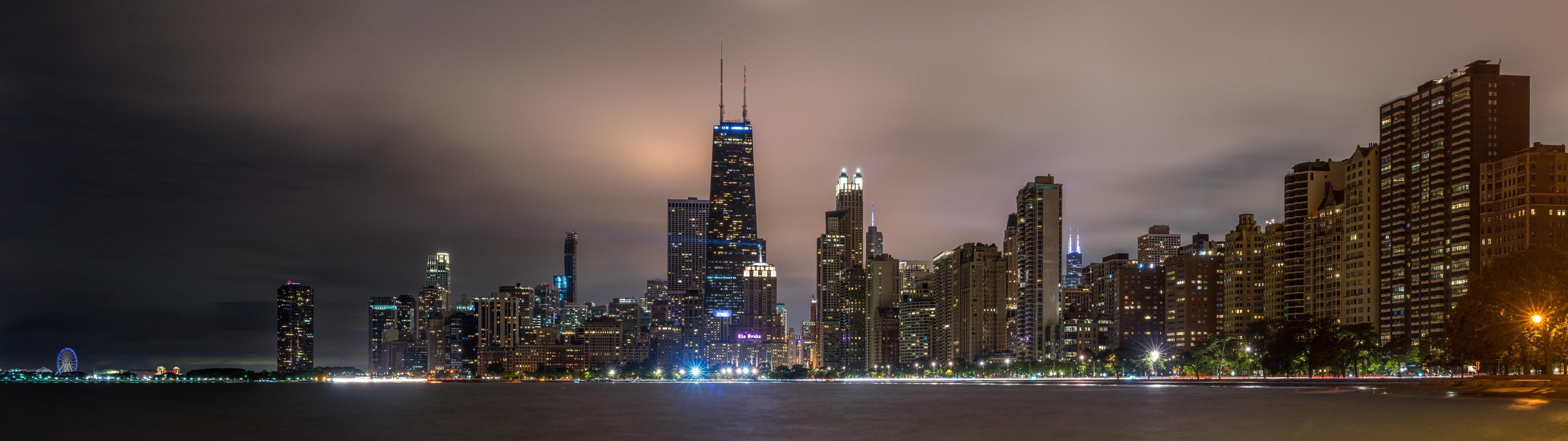 A city skyline at night with the water in front of it - 5120x1440