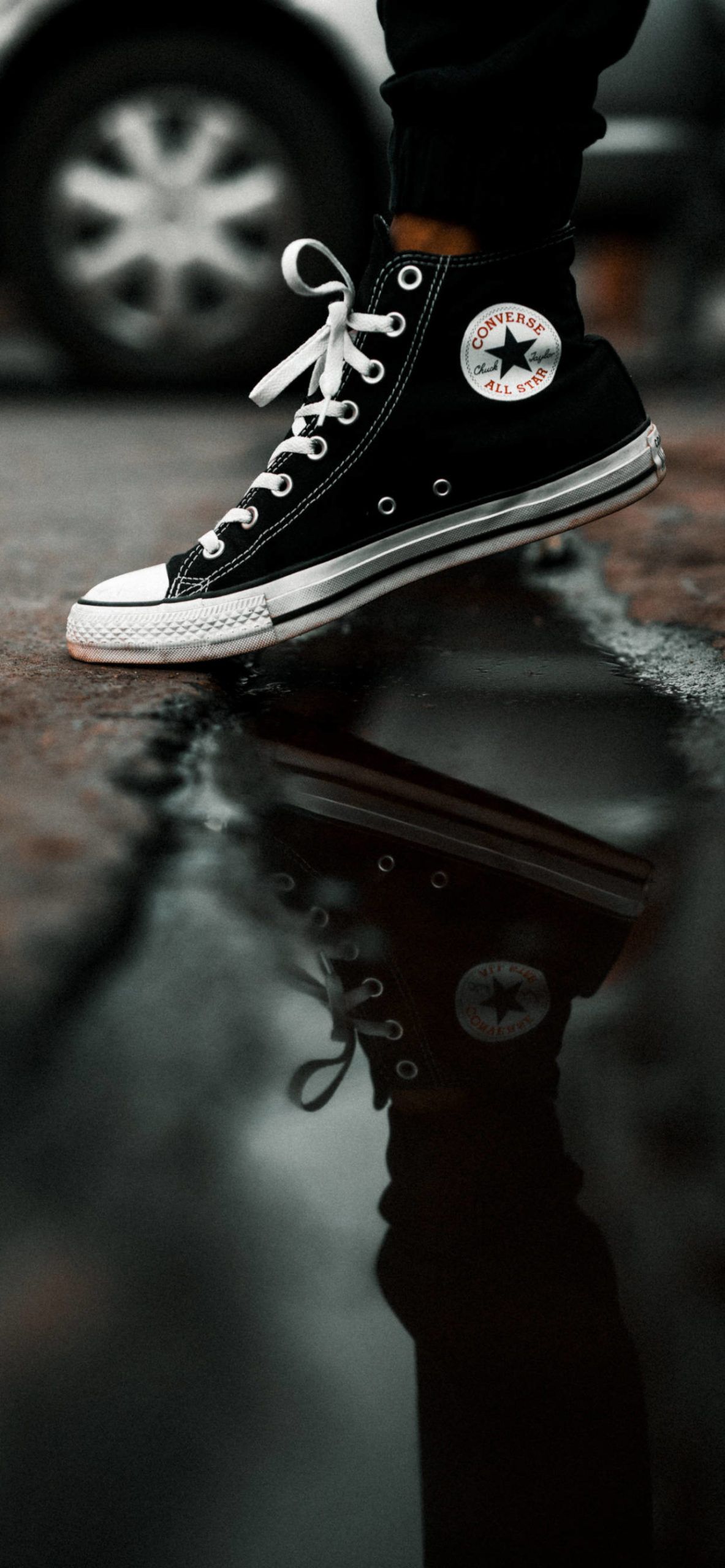 A person is standing on the ground with their shoes in mid air - Converse