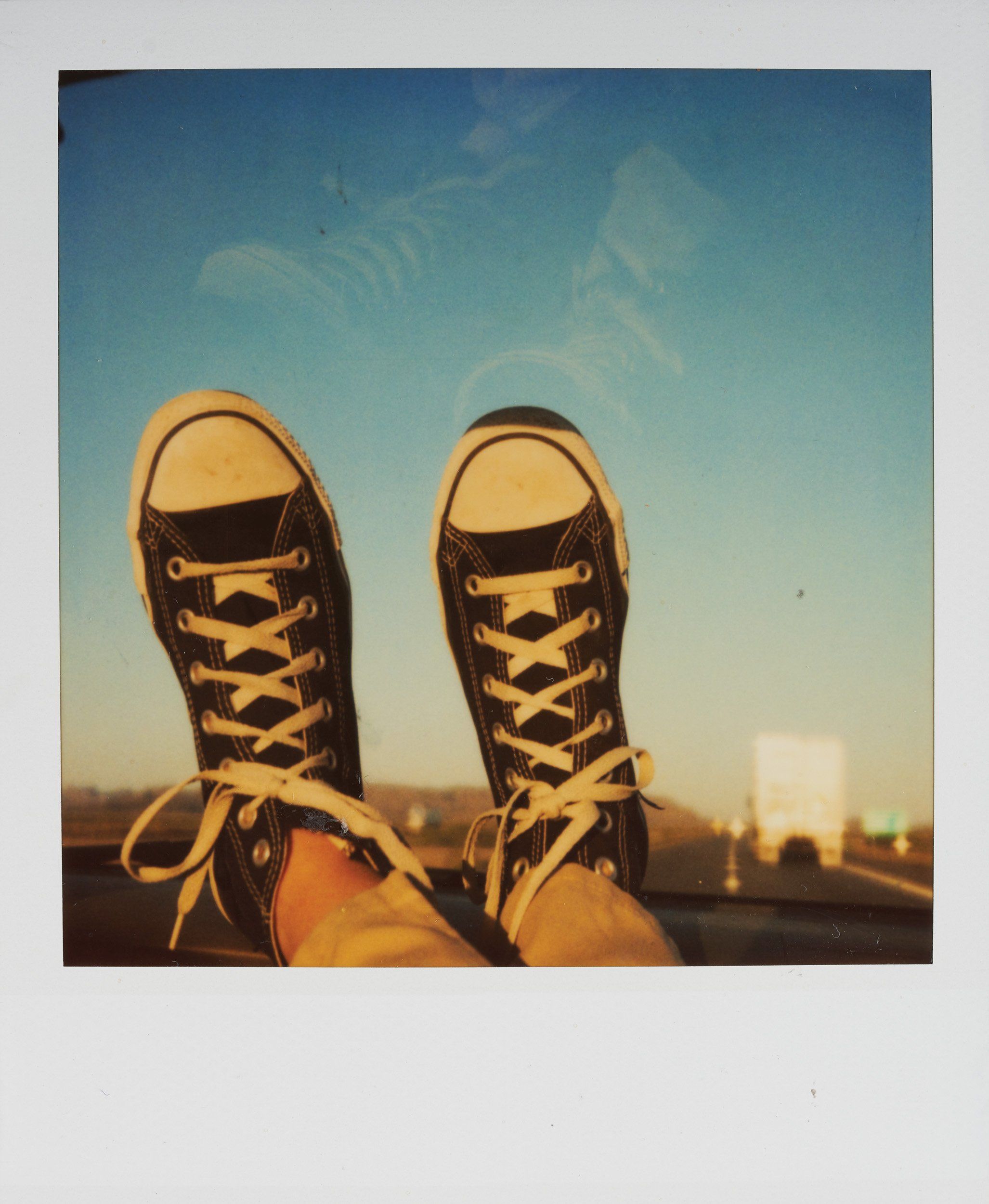 A pair of feet wearing converse sneakers are sticking out of a car window. - Converse, Polaroid