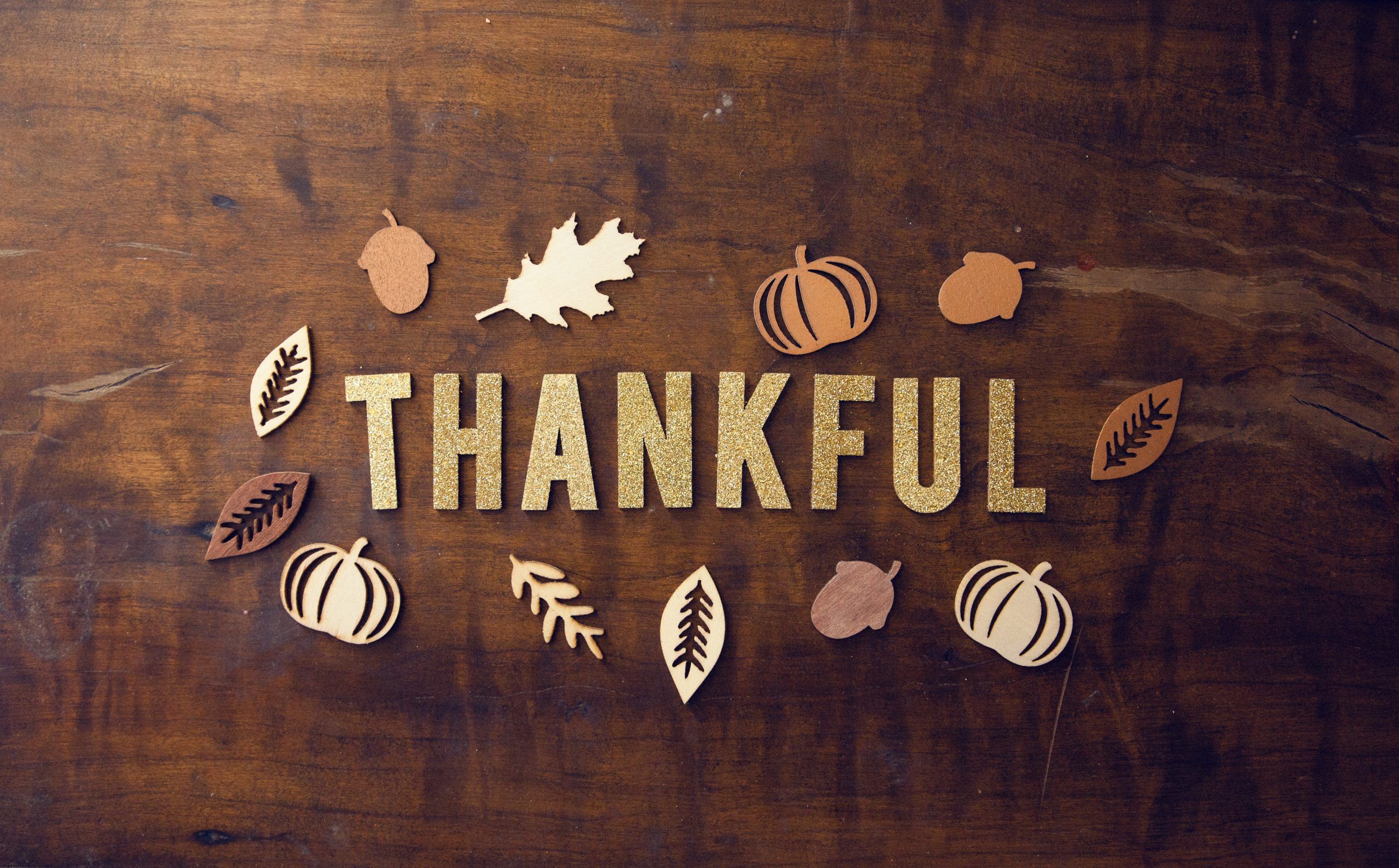 A wooden table with the word Thankful in the middle surrounded by leaves and acorns. - Thanksgiving