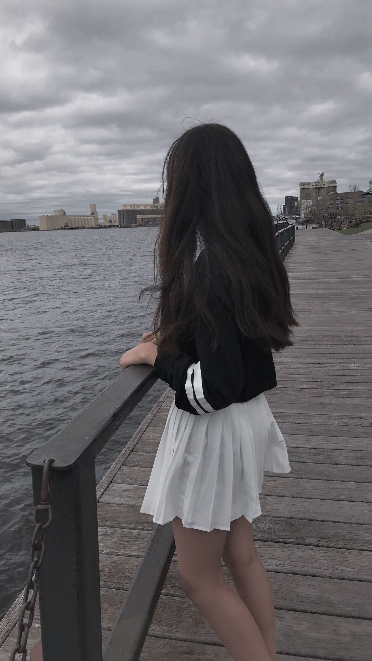 A woman with long black hair wearing a black and white jacket and a white skirt stands on a dock - Korean