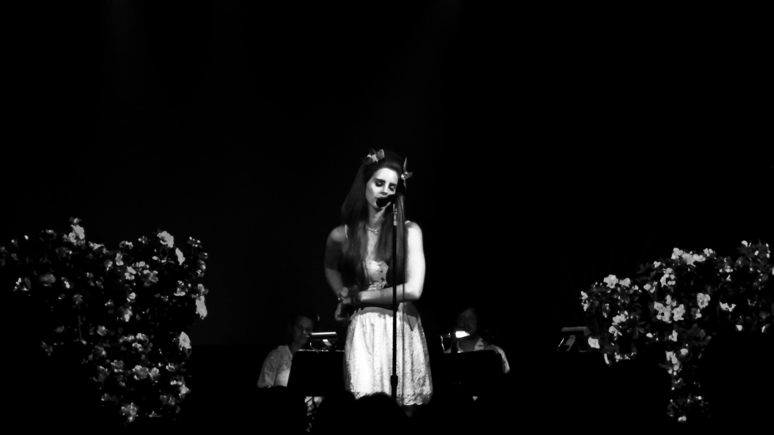 A woman singing on stage in black and white - Lana Del Rey