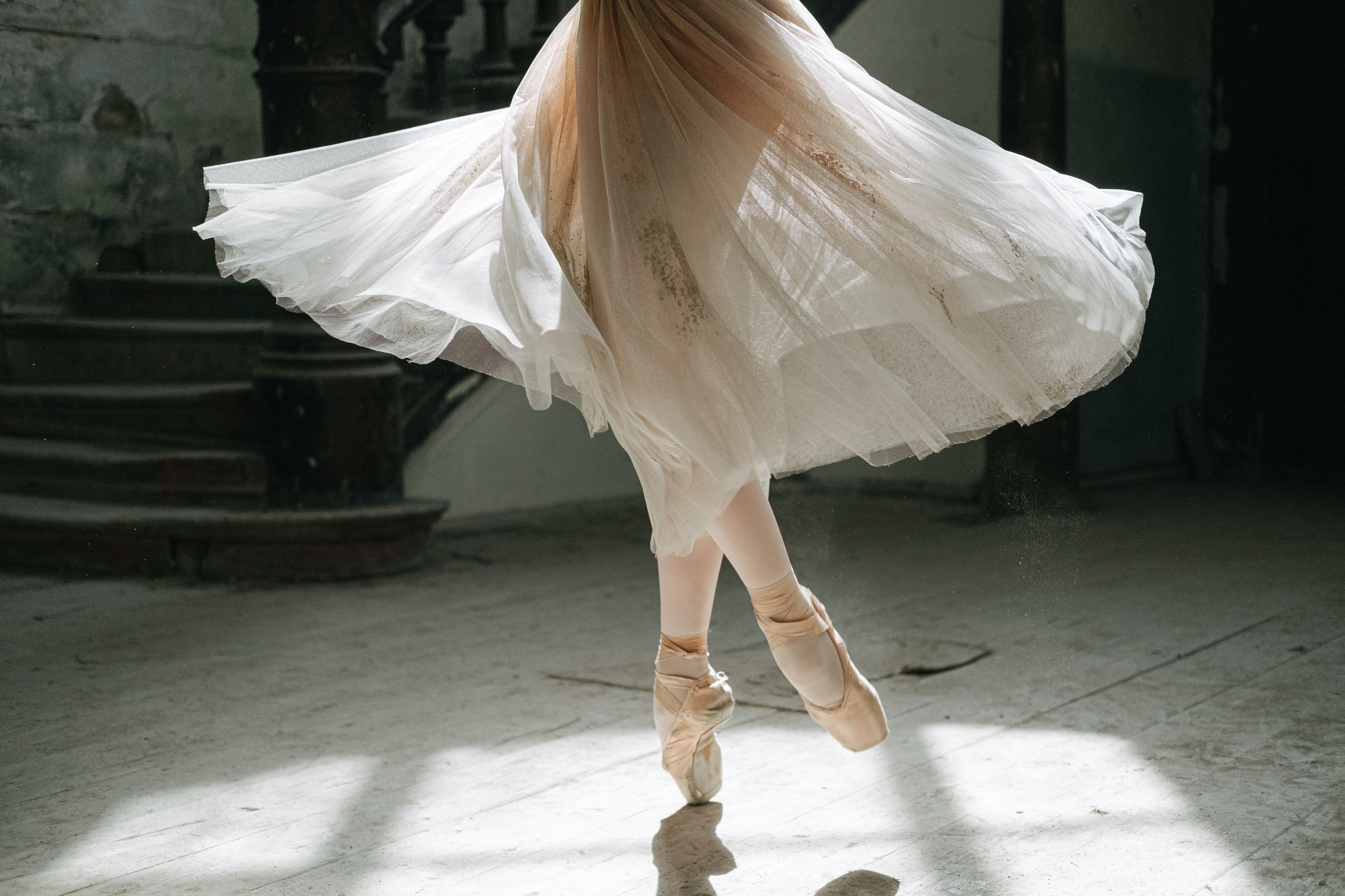 A ballerina in a white dress and pointe shoes dances in a sunlit room. - Ballet