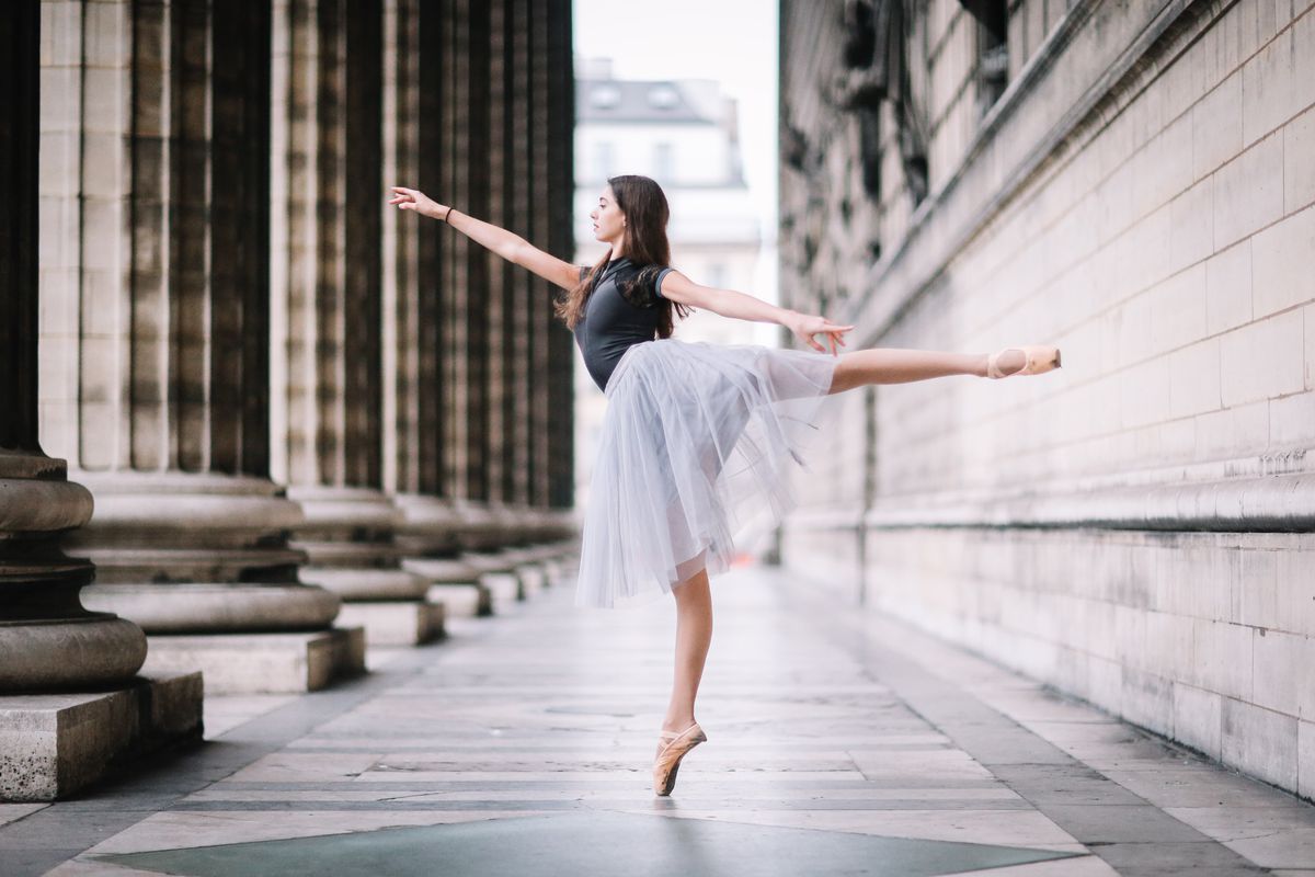 A woman in a white tutu dances in the middle of a street. - Ballet