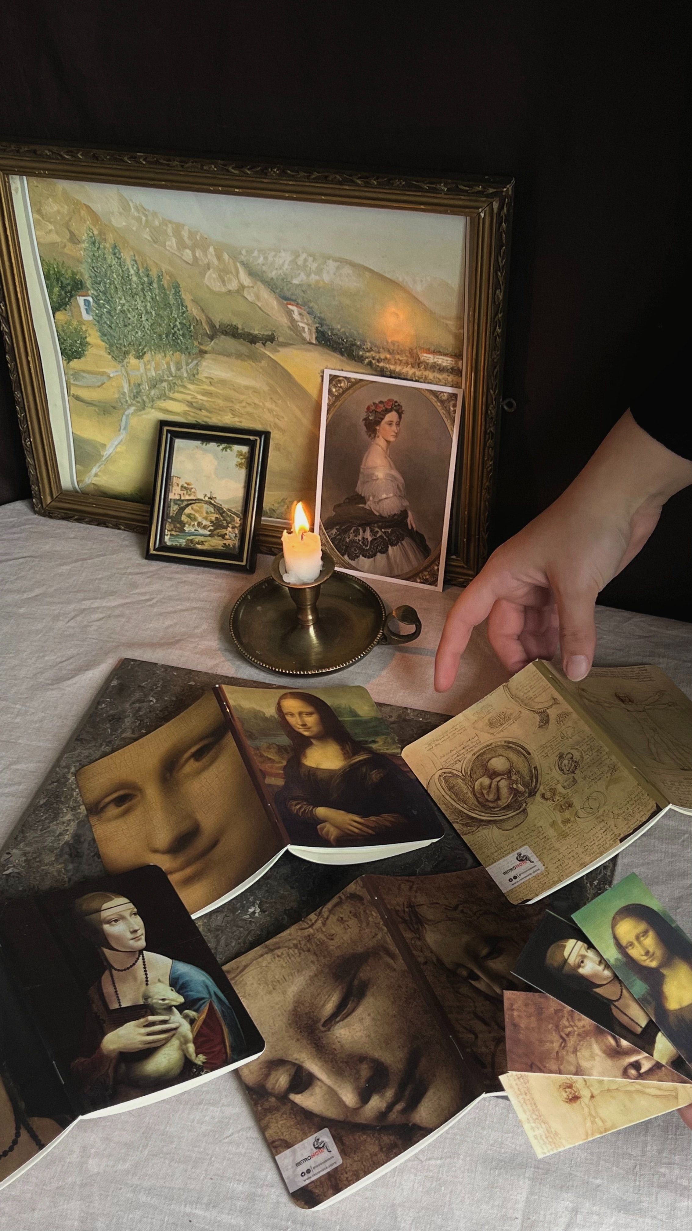 A person's hand reaches for a postcard of the Mona Lisa in front of a candle and a framed print of the painting. - Mona Lisa