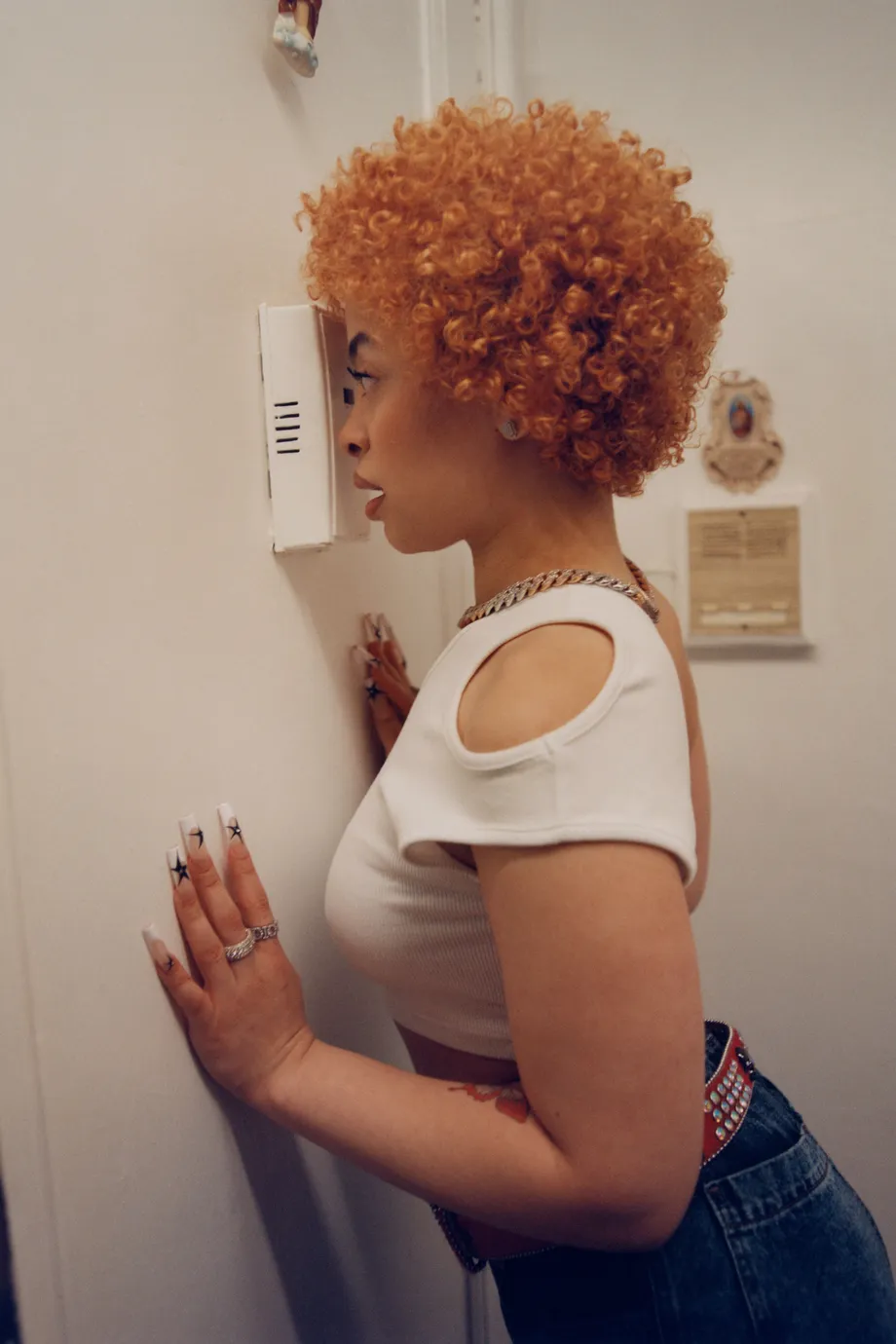 A woman with orange hair is looking through a peephole. - Ice Spice