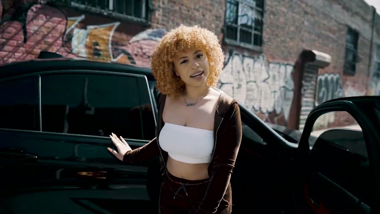 A woman in an orange wig stands next to her car - Ice Spice