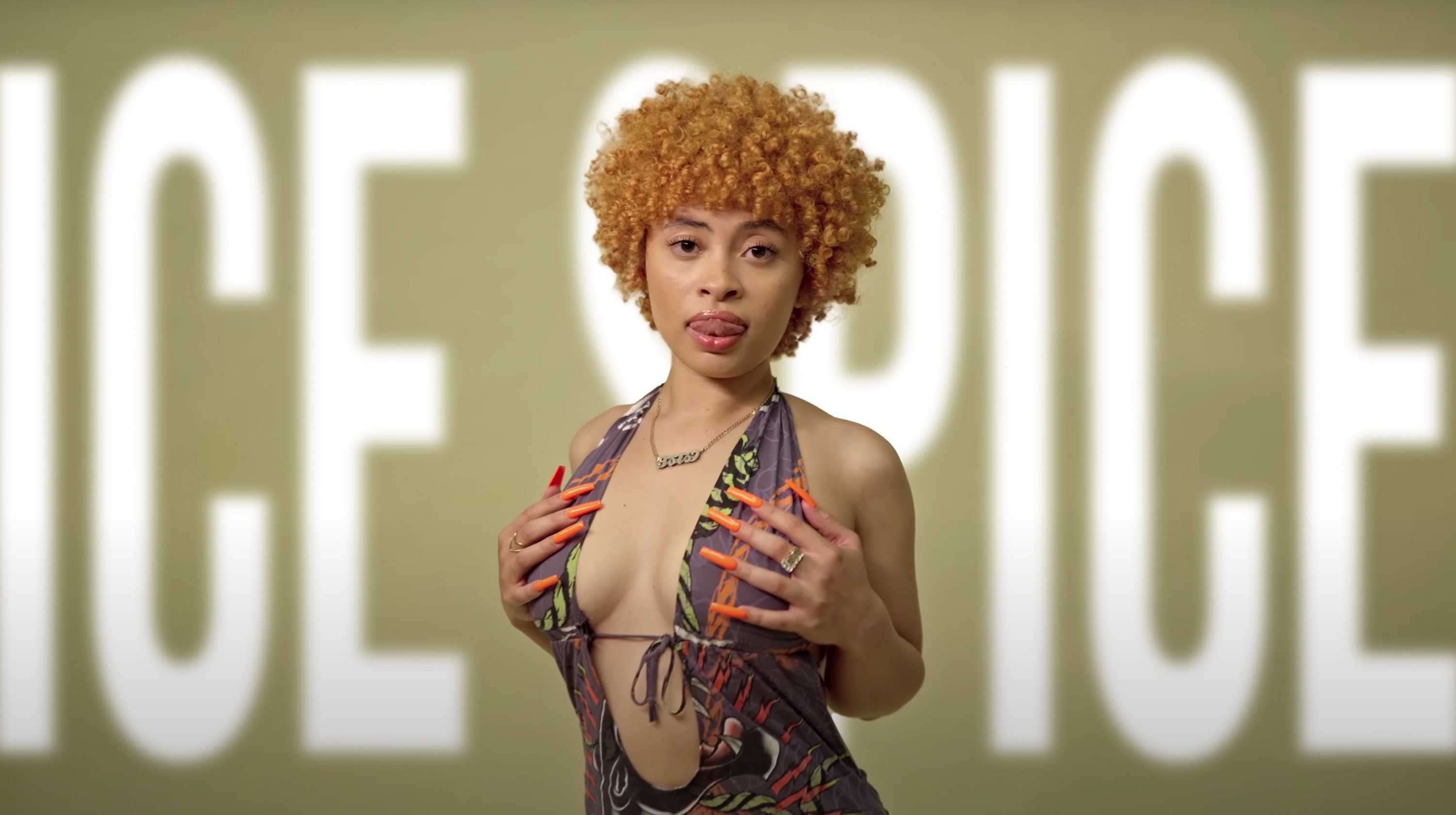 A woman with an afro and a colorful top stands in front of the words 