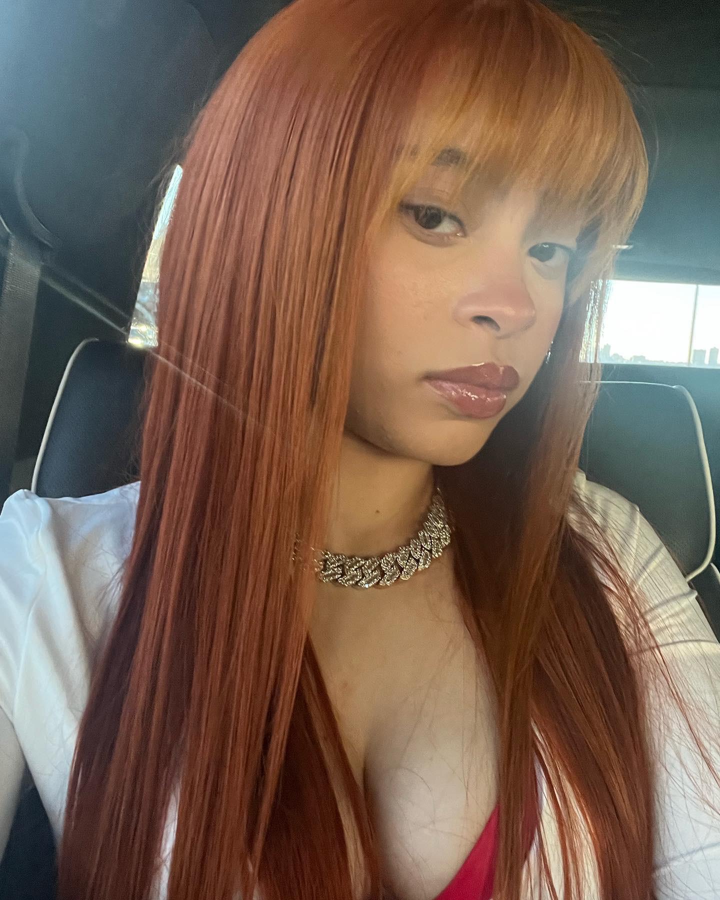 A woman with long red hair in the back seat of her car - Ice Spice