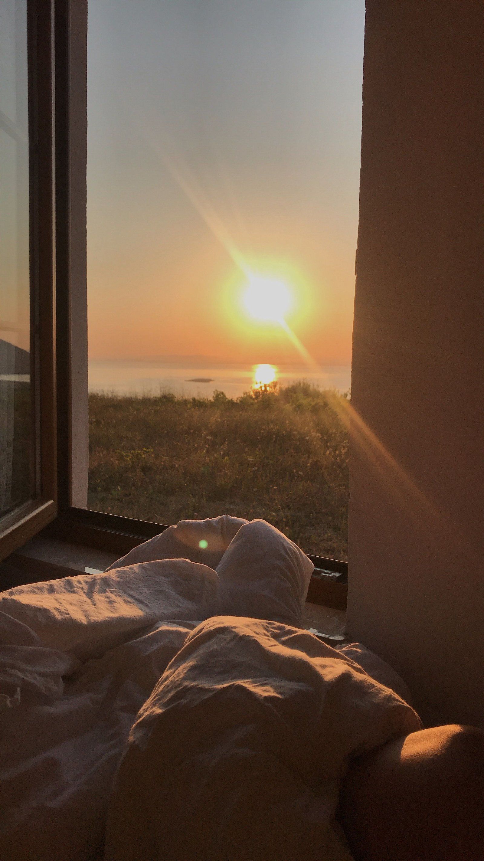 A view of the sun setting over the ocean from a bed. - Sunshine