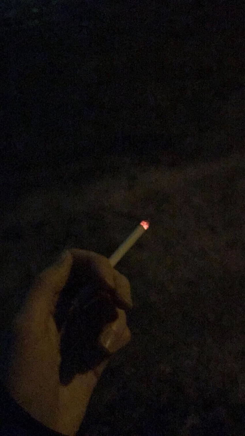 A person is holding a lit cigarette in their hand. - Smoke