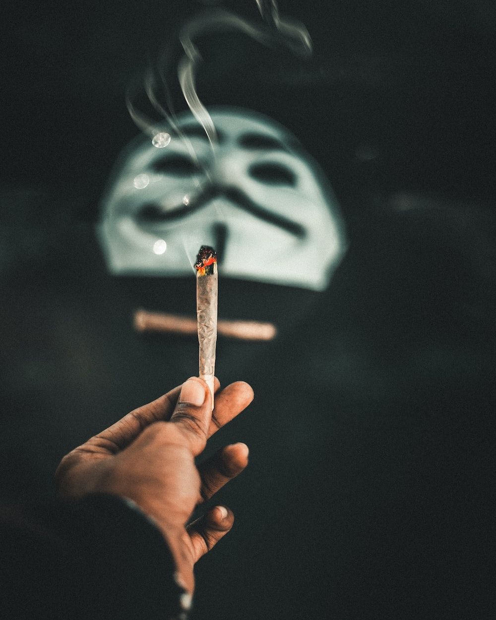 A person holding a lit cannabis joint in their hand - Smoke