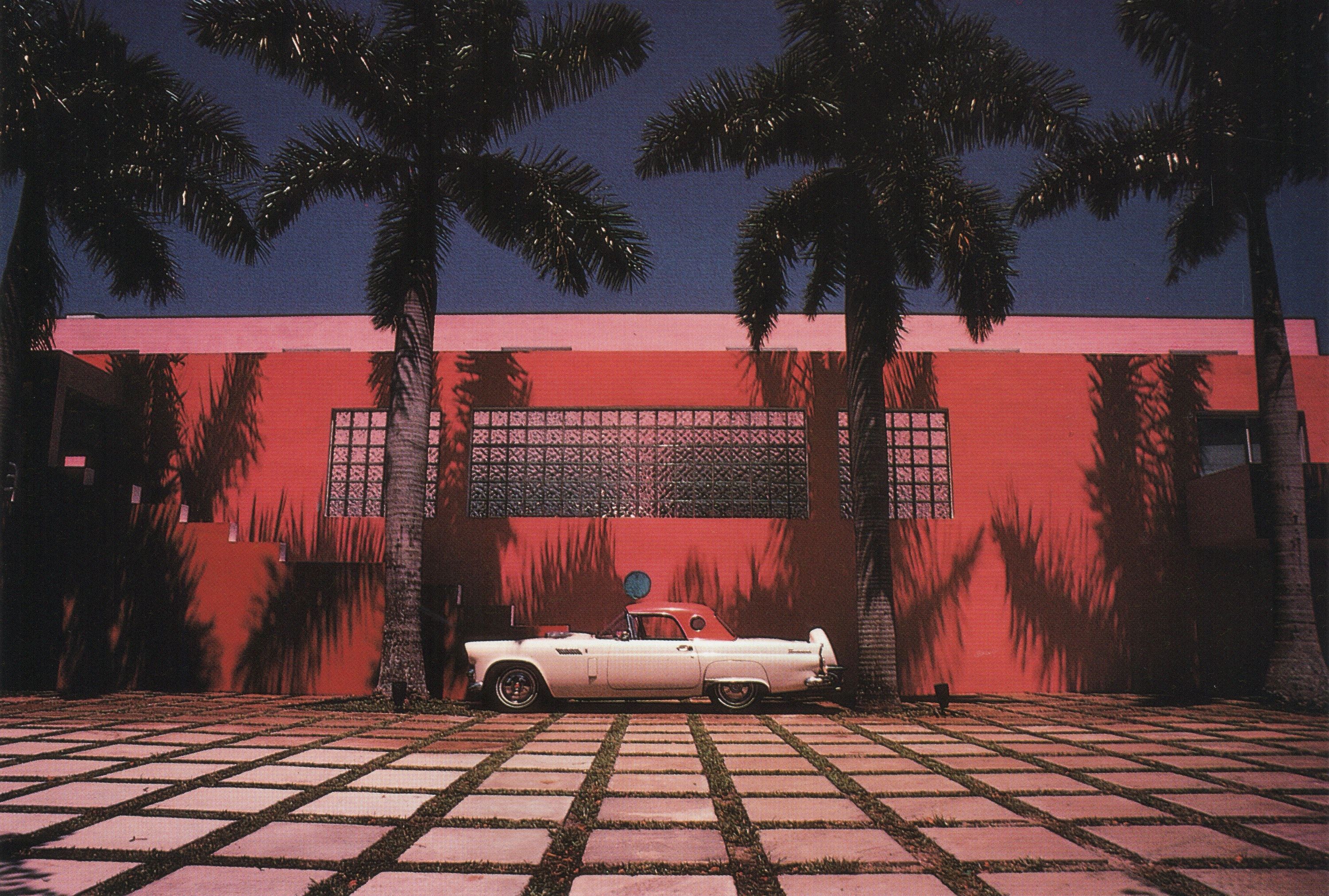 A red Thunderbird car is parked in front of a red building. - Miami