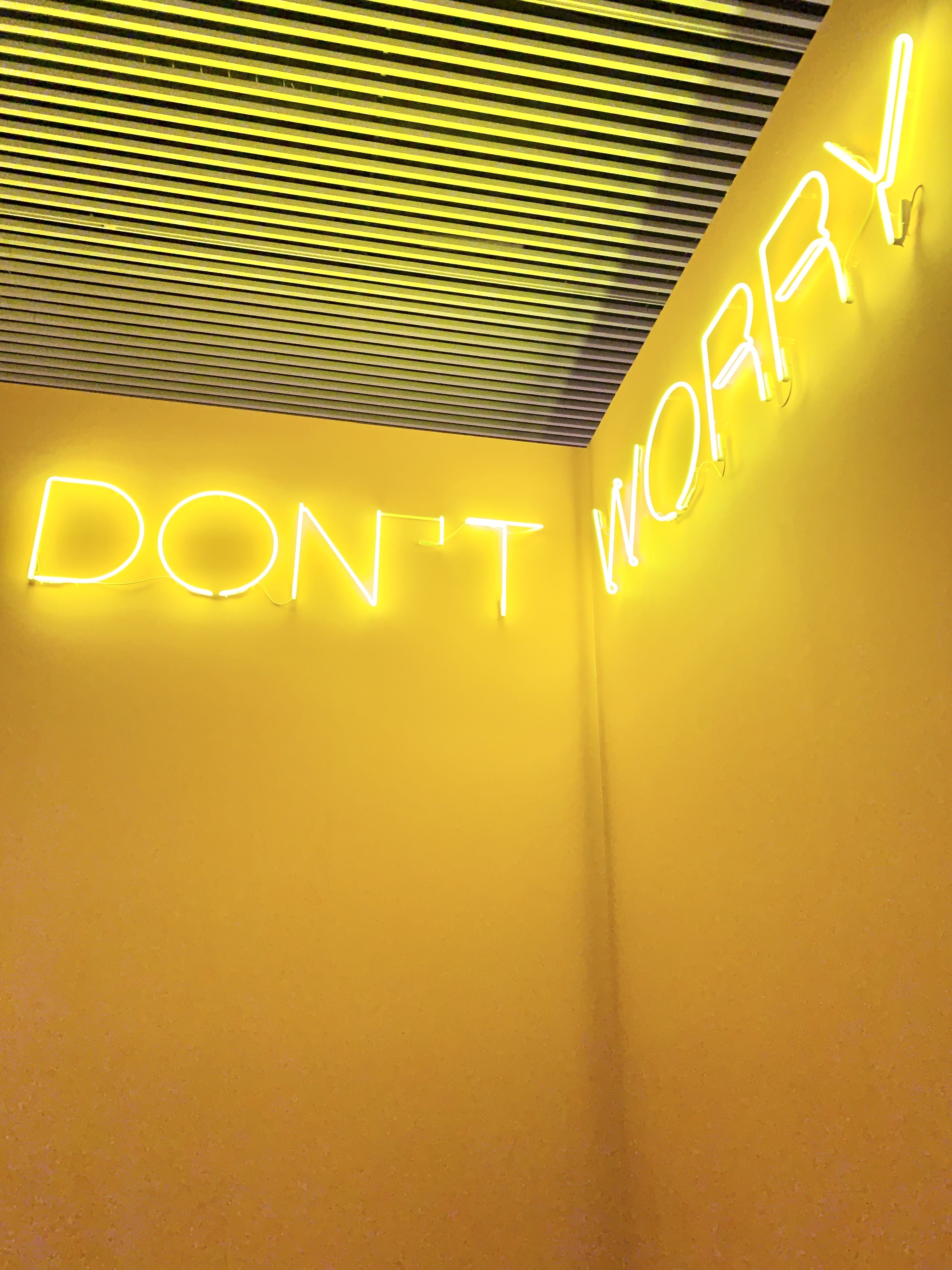 A 'don't worry' sign in neon lights on a yellow wall. - Neon yellow