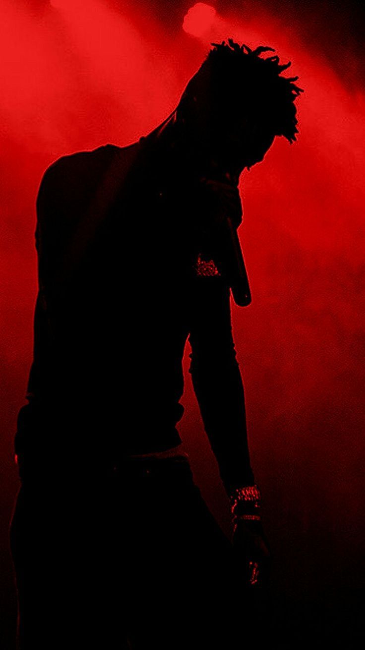 A silhouette of a man on stage in front of a red light. - 21 Savage