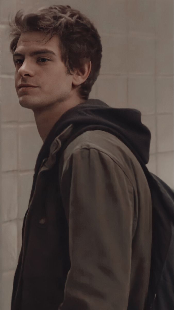 A young man with a backpack standing in front of a wall - Andrew Garfield
