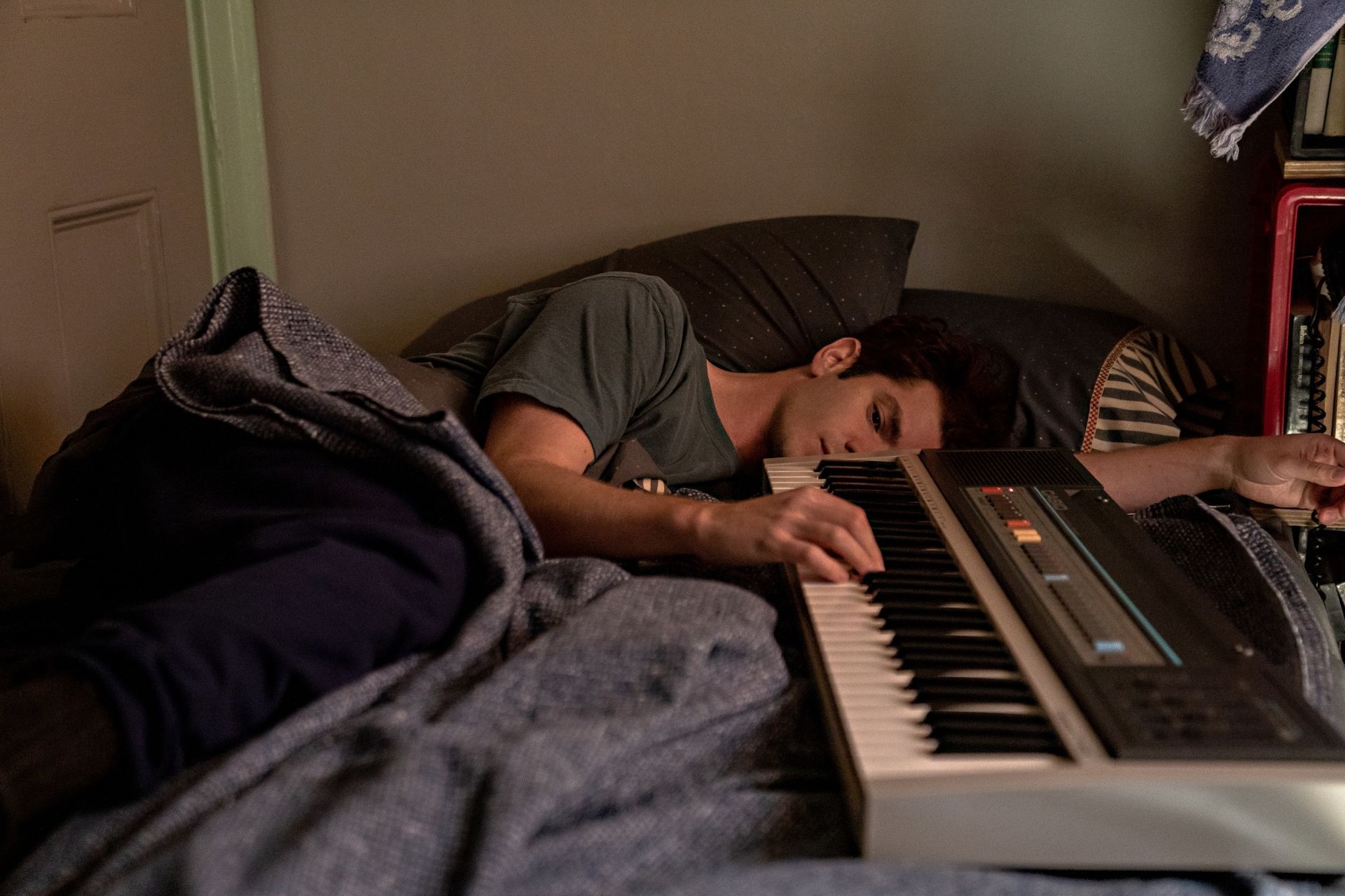A young man is asleep on a bed with his arm on a keyboard. - Andrew Garfield