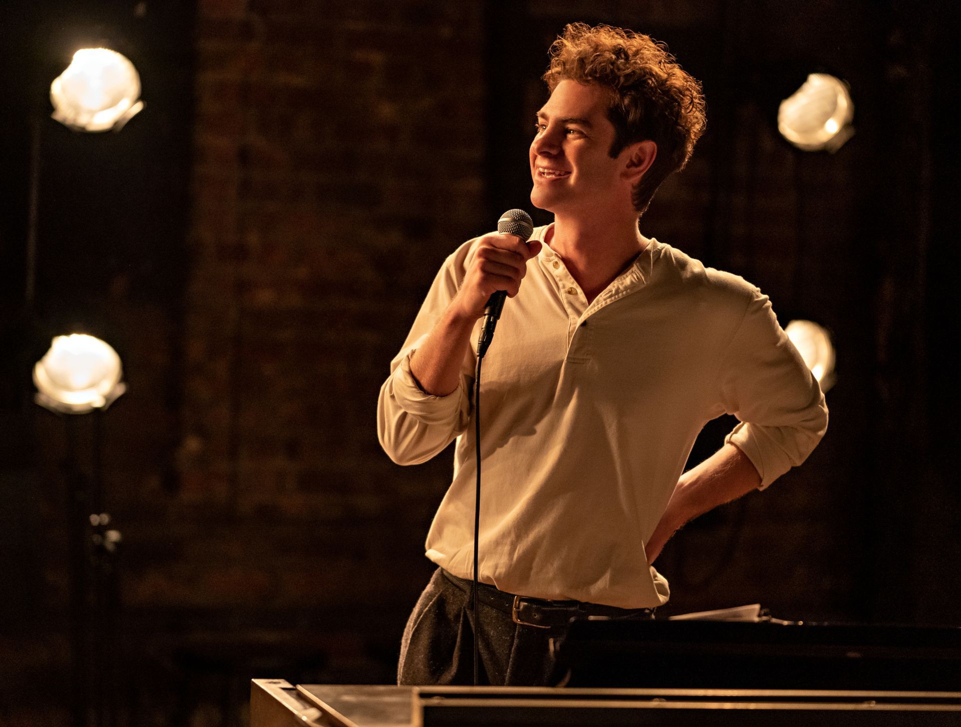 Andrew Garfield in a white shirt, holding a microphone and smiling. - Andrew Garfield